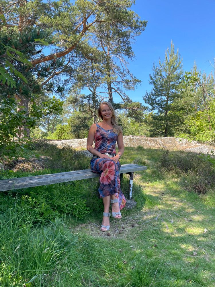 This is me. I'm wearing a purple and pink dress. I'm sitting on a bench in the forest in the summer.