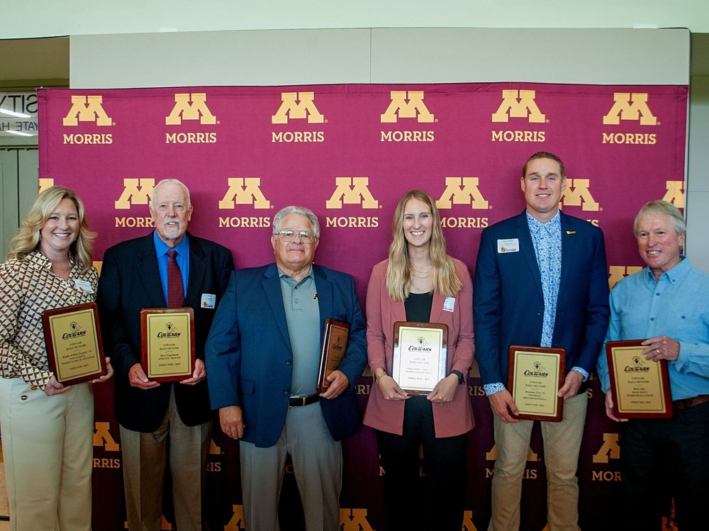 Group of six individuals holding awards, standing in front of a University of Minnesota Morris banner.