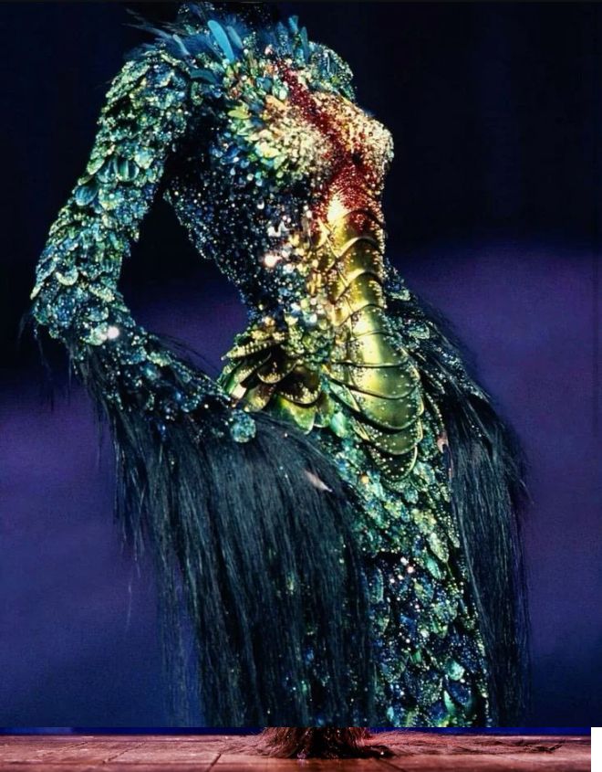 a long sheath dress with a gold articulated corset adorned with “scales” and embellished with feathers, crystals, and horsehair at the end of the sleeves 