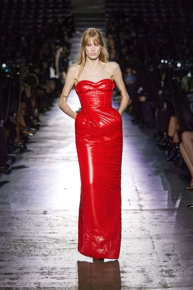 A runway model wearing a sleeveless heart neckline bubble hip red leather dress
