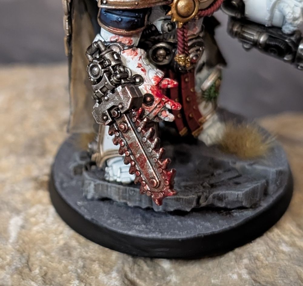 A close up of the huge chainfist on his right arm, covered in blood and gore.