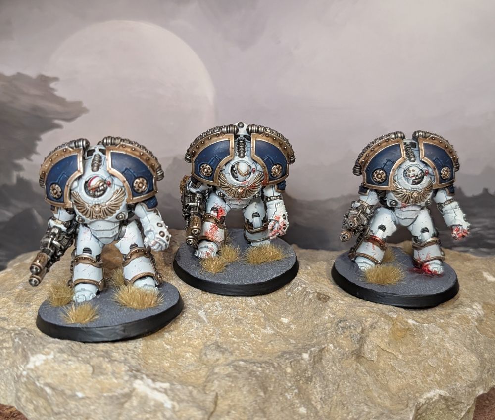 Three hulking Saturnine Terminators, in the white and blue armour of the World Eaters, with brass trim.