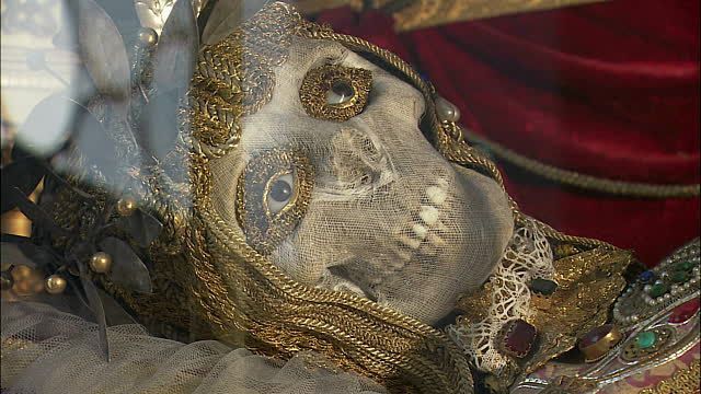 Skull (possibly whole skellington?) lying inside elaborate Euro renaissance outfit, with jeweled "eyes" added