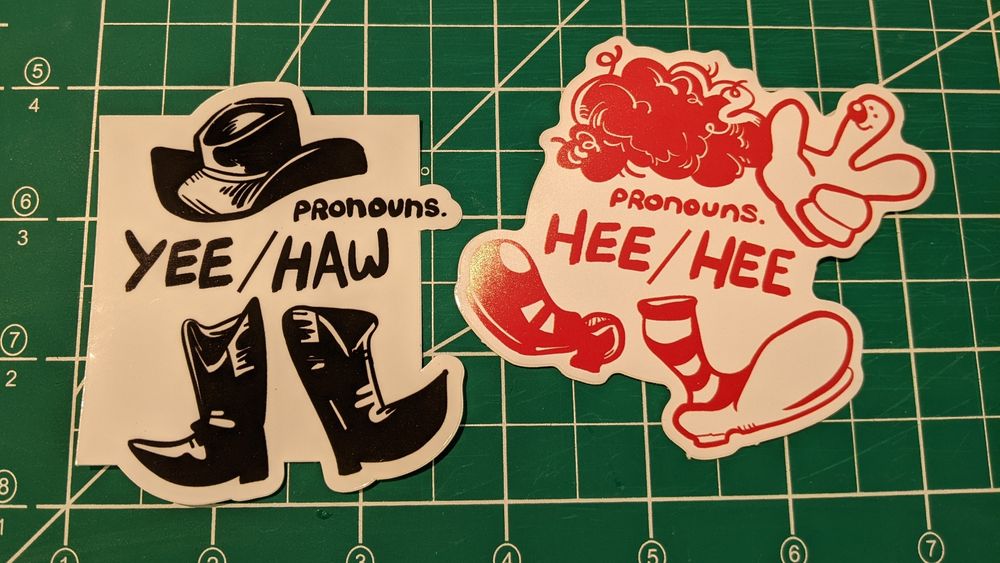Two stickers each about 3x3". The first is black and white, a cowboy hat and boots around the text, "Pronouns. Yee/Haw." The second is red and white, stripy socks and large clown shoes, wig and glove with a clown nose and smile surrounding text that reads, "Pronouns. Hee/Hee."