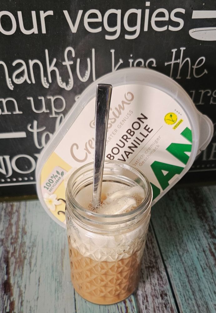 Glas mit Vanilleeis und ein Cappuccino, dahinter eine Box Bourbonvanilleeis vegan.