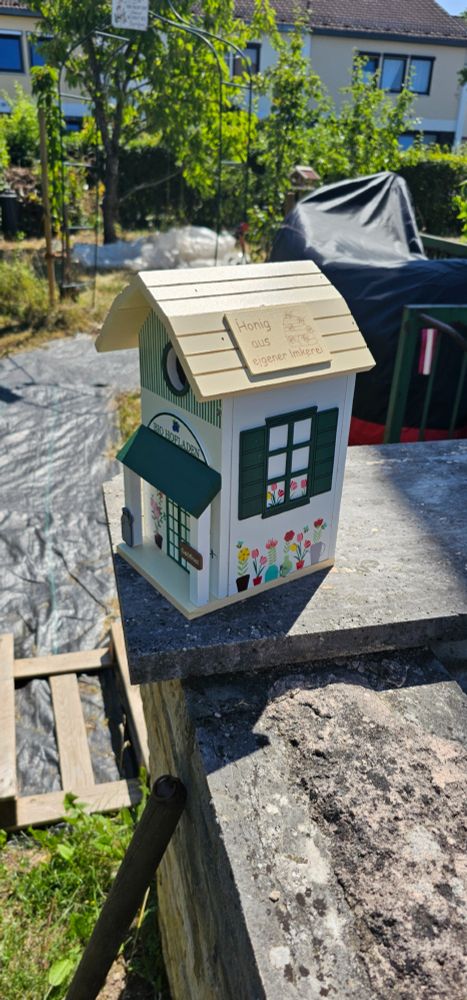 Vogelhäuschen auf einer Mauer. Im Hintergrund ist der Garten sichtbar.