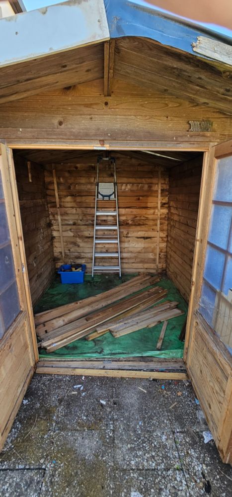 Alte Hütte mit Holzlatten auf dem Boden und eine Leiter im hintern Bereich.