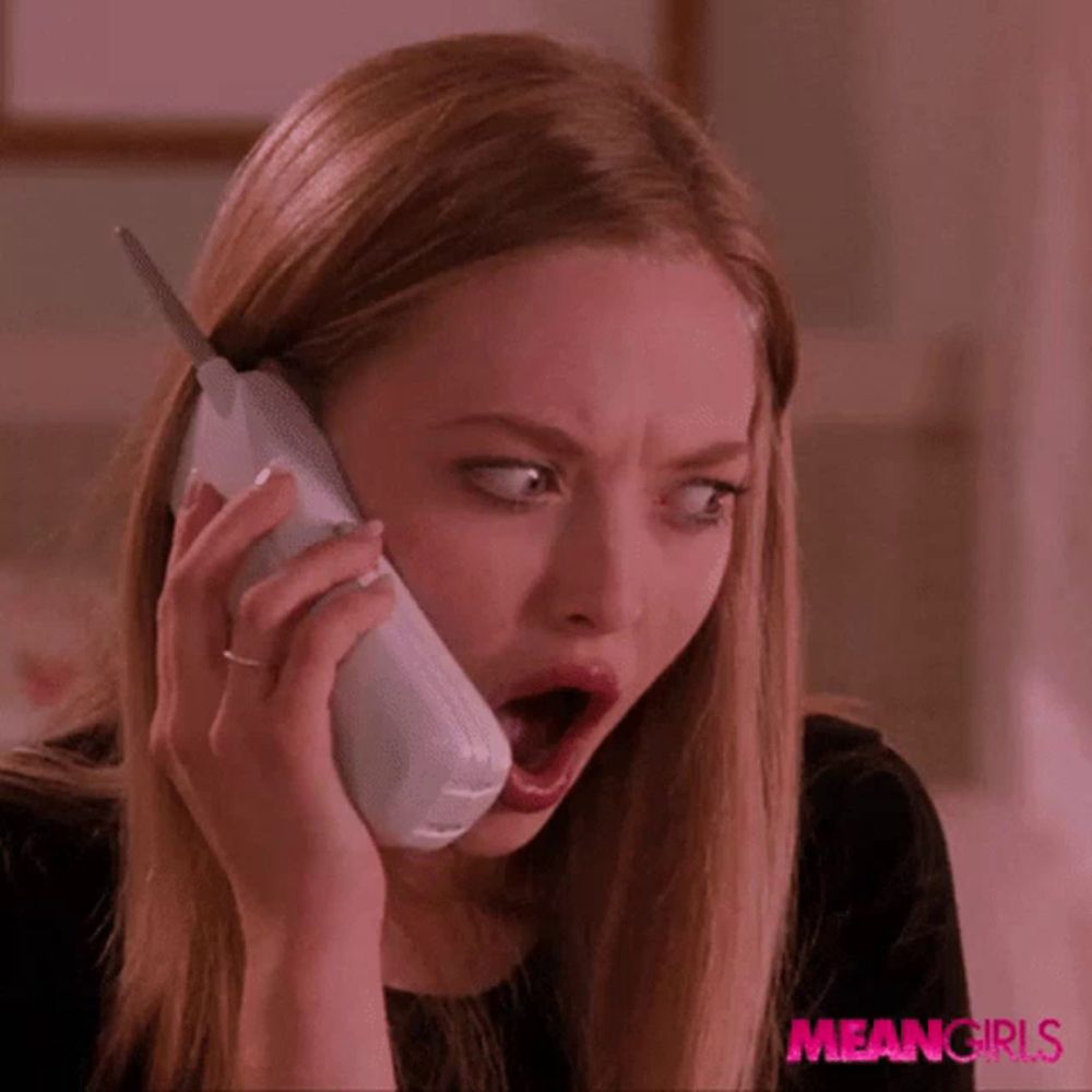 a woman with a surprised look on her face is talking on a phone with meangirls written on the bottom right