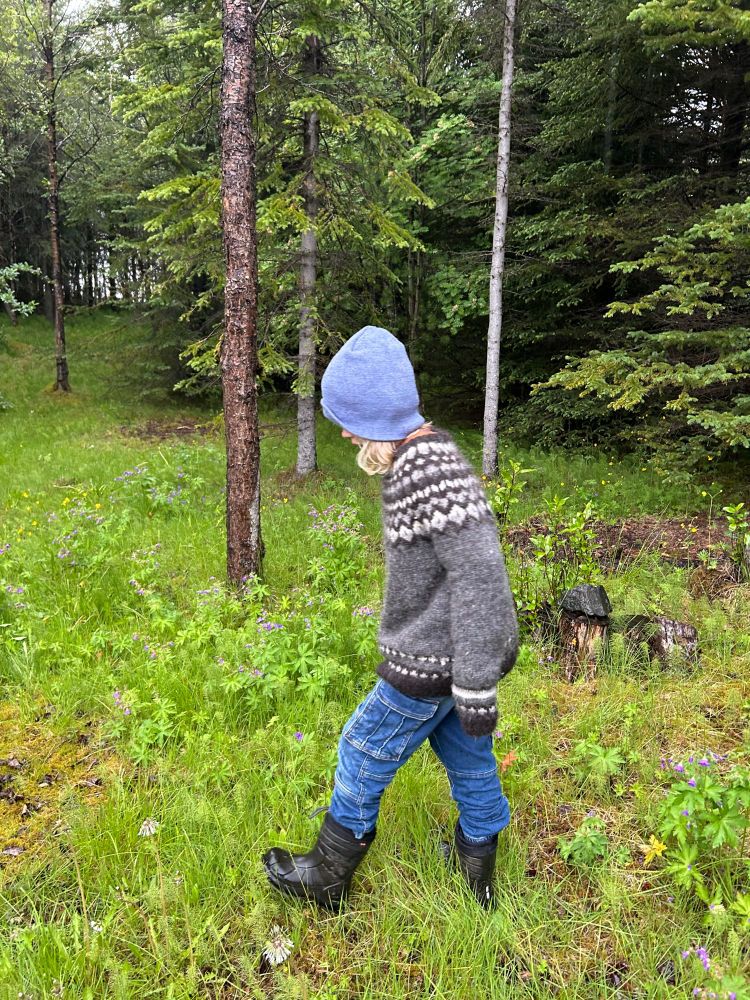 Boy in knit cap, wool sweater, and boots walking in the woods.