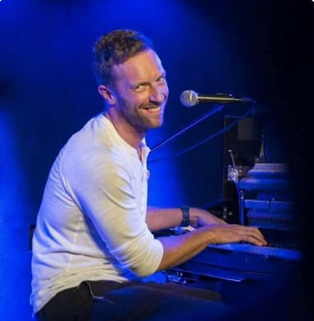 Chris Martin of Coldplay playing the piano and smiling 