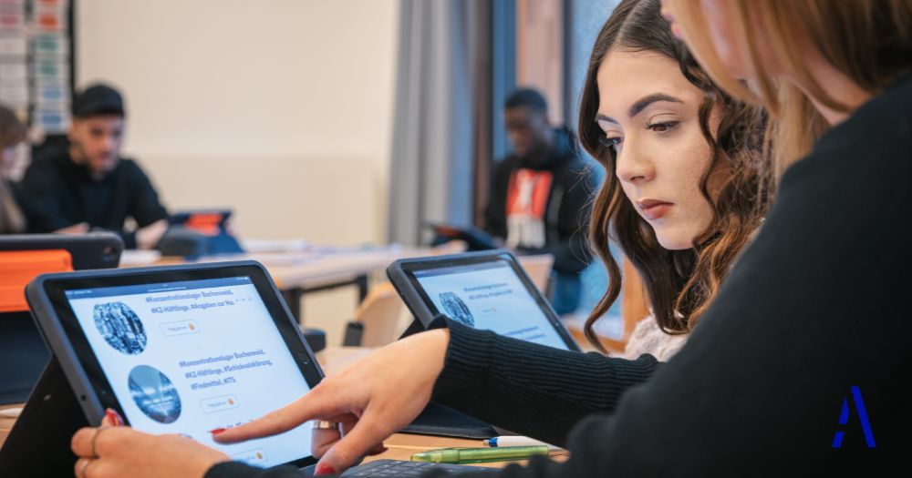 Two pupils working together on a tablet in class. Content from the #everynamecounts project can be seen on the tablet. Other pupils are sitting in the background.
