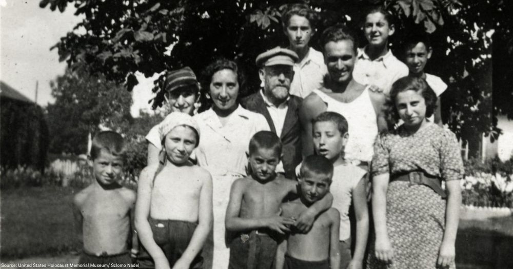 Black-and-white photograph of Janusz Korczak and Sabina Lejzerowicz standing together with children and staff from the orphanage he ran in Warsaw. They are standing outside, with trees, two houses, and a meadow visible in the background.