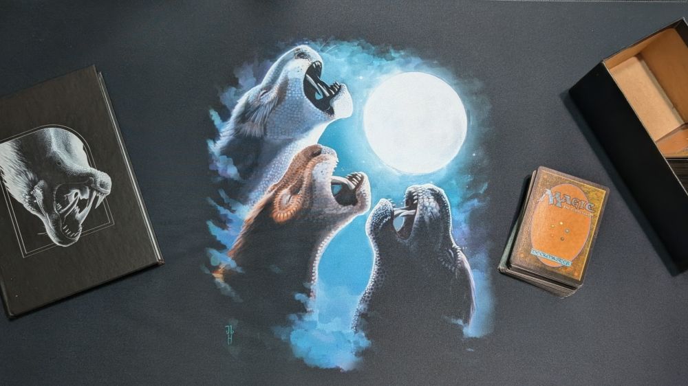 Desk mat with three gorgonopsid moon on it, a journal with Innovate Rubidgea on it. Some magic cards sit off to one side. 