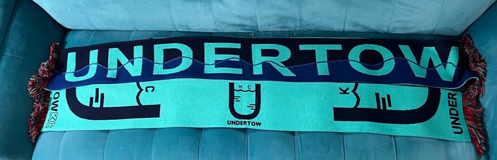 A picture of the first Undertow scarf, taken from both sides. Top: “Undertow” written with a wave through the bottom half of the word. Bottom: Undertow logo