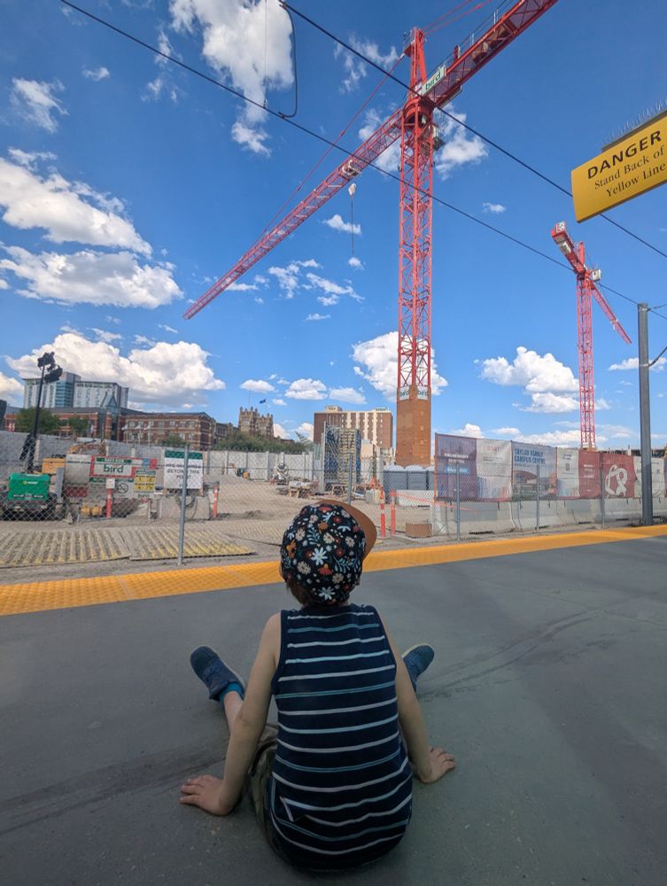 Child watching a big constructions site and two red cranes