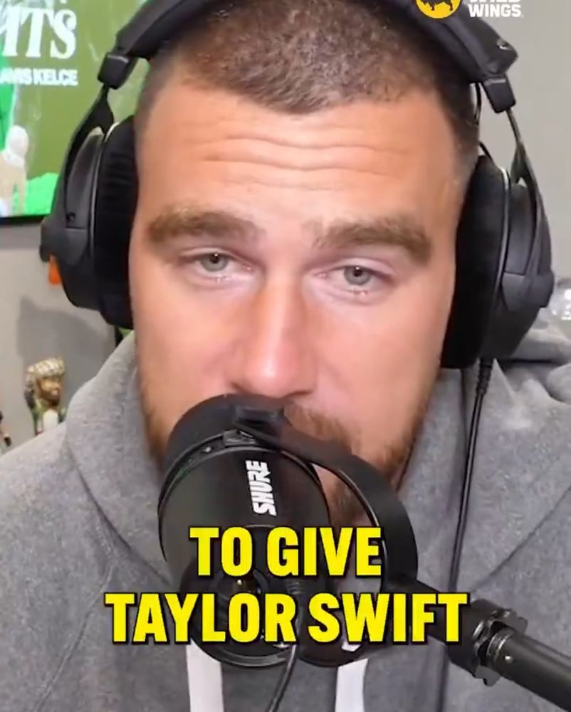 Travis Kelce on the New Heights podcast wearing a grey hoodie and headphones with a caption in yellow that says “to give Taylor swift” 