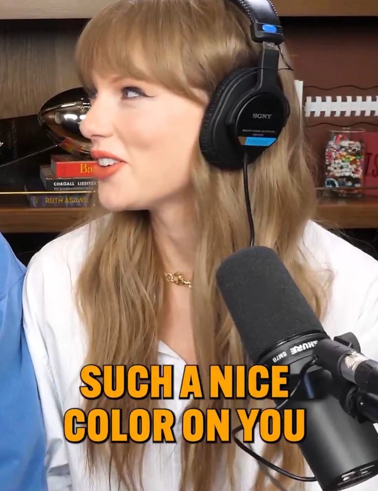 Taylor Swift on the New Heights podcast wearing a white shirt and headphones with a caption that says “such a nice color on you” 