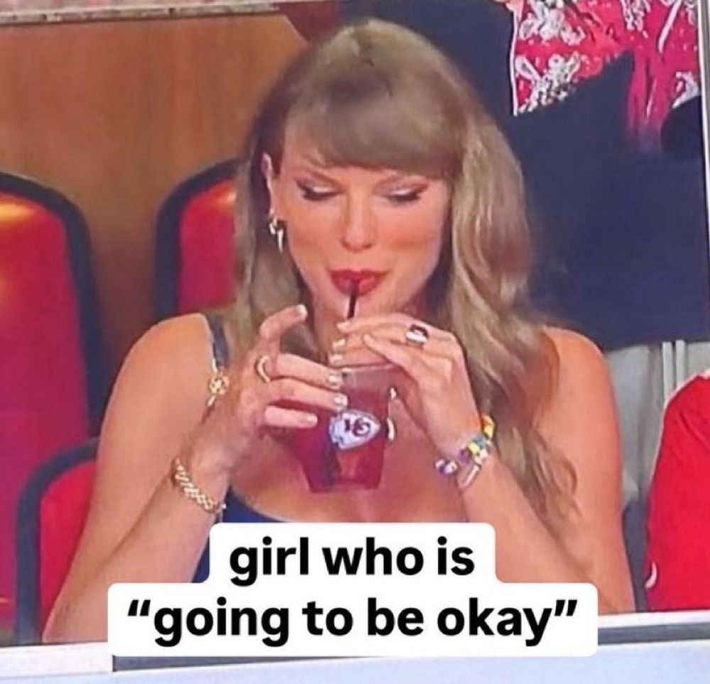 taylor swift at a chiefs game drinking out of a cup with a caption below that says “girl who is going to be okay” 