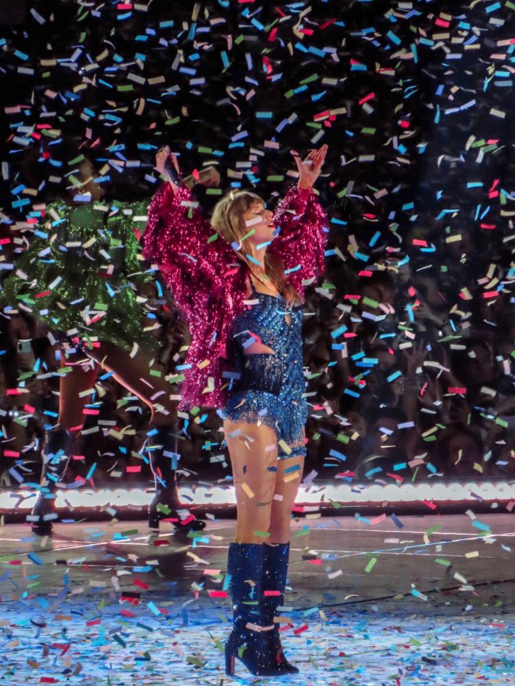 taylor swift onstage at the eras tour in chevron blue bodysuit and magenta tinsel jacket with confetti coming down 