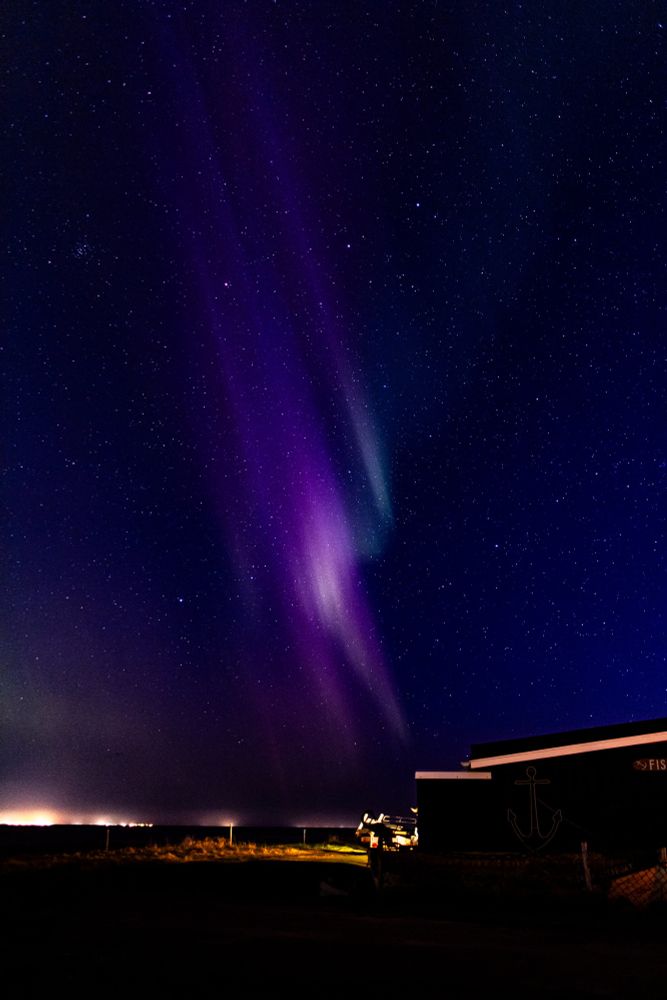 Aurora borealis forms the shape of a ghostly figure dissolving into the heavens above an unidentified human structure.  