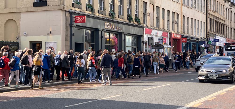 People crowded at a bus stop - blocking movement along the pavement and access to a restaurant.
People forced to walk in the road whilst buses and cars drive by, all due to incompetent and cowardly Councillors unwilling to take responsibility. 