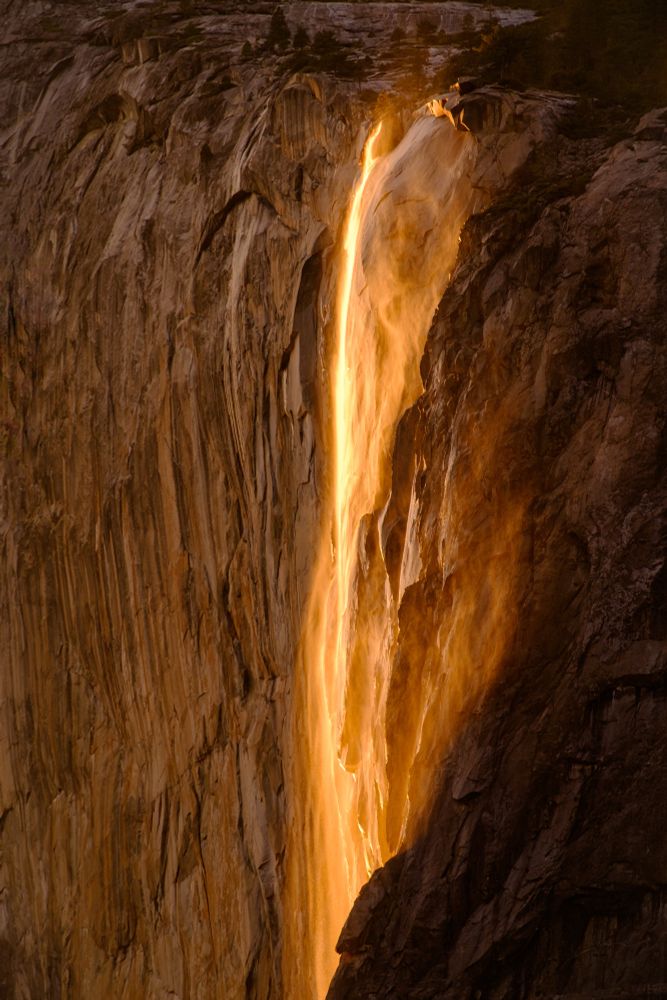 A stunning waterfall cascading down a rocky cliff, illuminated by warm, golden light, creating a dramatic and ethereal effect.