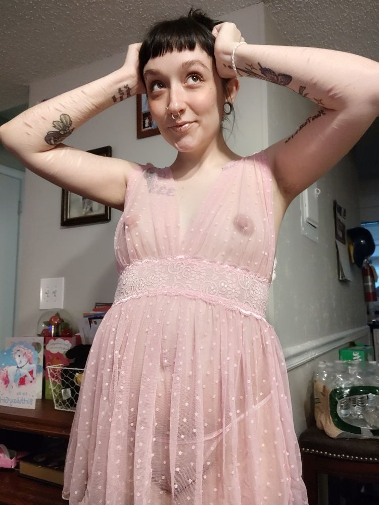 a photo of rad in pink sheer lingerie, that is babydoll style with a pink thong. their arms are up on their head and you can see their nipples and tummy through the lingerie. 