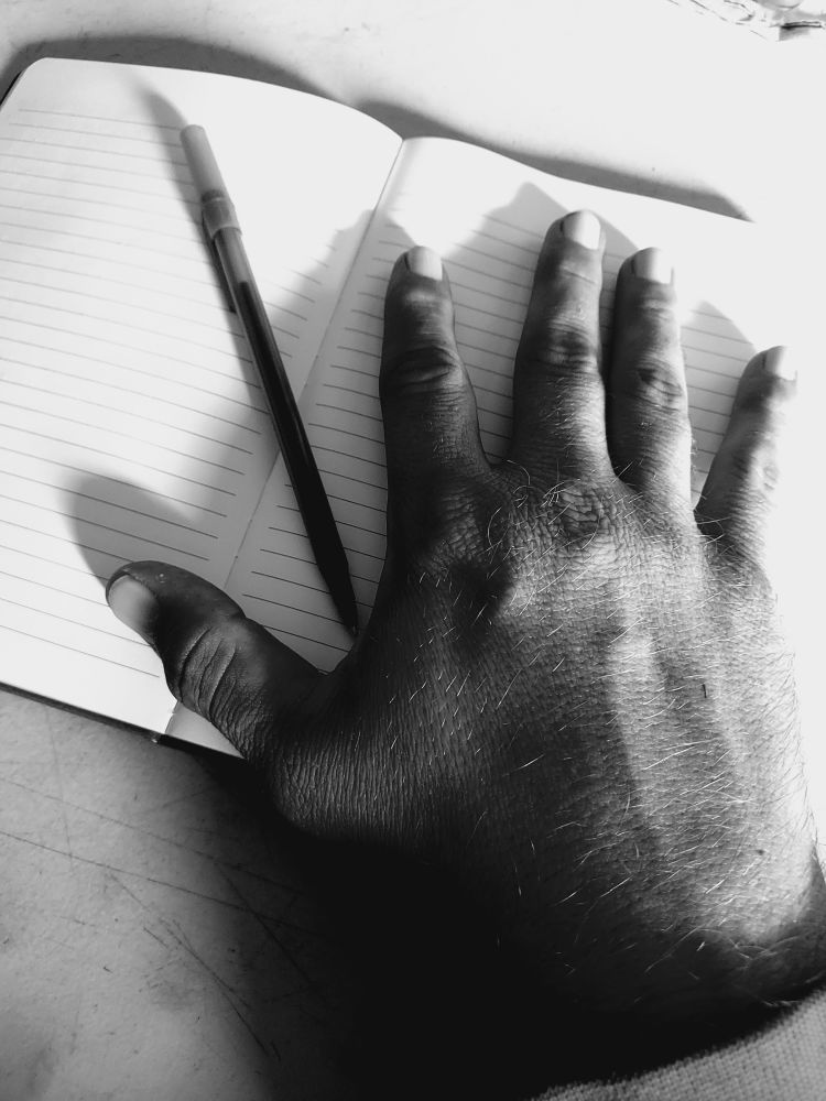 A right hand on a journal with a pen. In black and white.