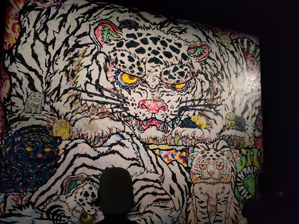 Das Bild selbst zeigt eines der vier Wundertiere: Blauer Drache, Roter Vogel, Weißer Tiger, Schwarze Schildkröte – die die vier Himmelsrichtungen symbolisieren. Der Tiger ist diesmal tatsächlich weiß.Er hat wie der Drache sehr runde *googelige* Augen. Er hat auch zwei kleine Tigerbabies eines spielt, das andere schaute müde dieBetrachter*innen an. Der weiße Tiger, der für h die schwarze Fellmusterung ein bisschen wie ein Zebra wirkt, also er sehr müde wäre.