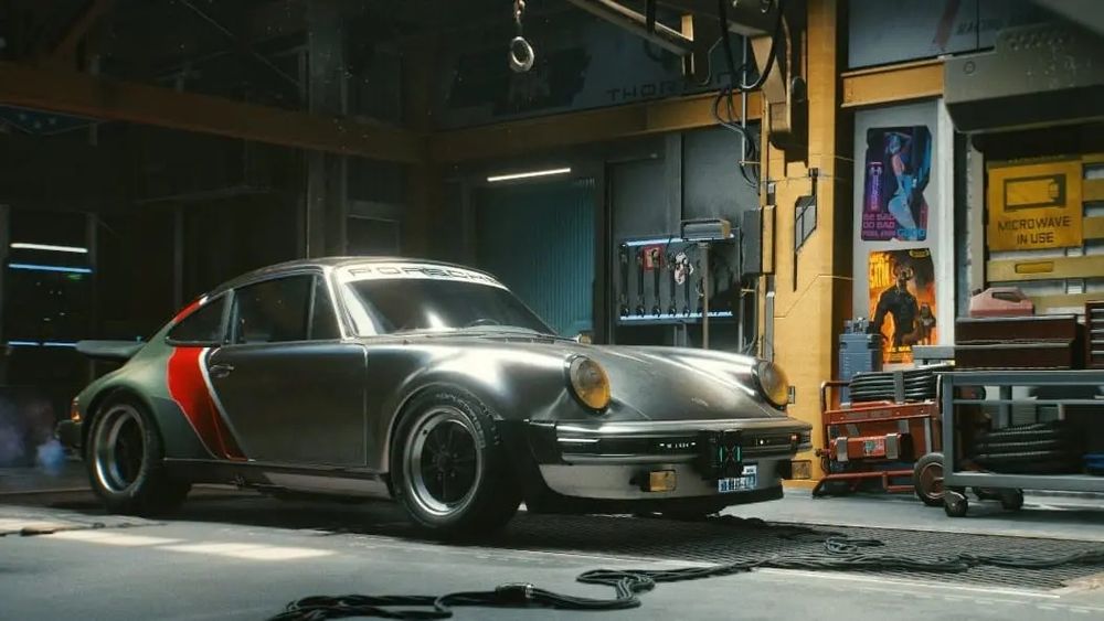 Ein Porsche 911. In einer Werkstatt Das Auto ist Silber und hinten rot/oliv. Es steht auf einer Hebebühne. An den Betonwänden sind gelbe Metallstreben und man sieht Werkzeug herumstehen. Das Auto ist Johnny s Porsche aus Cyberpunk 2077