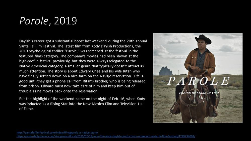 This slide contains one photo of Parole, a western set on a reservation.  Edward Chee is the main character and in the photo he is on his horse outside on the farm.  You can see his house in the background.  His horse is brown with a white stripe down its nose. Edward is wearing a white t-shirt under a blue shirt long sleeved shirt and blue vest with a brown leather jacket and a black felt cowboy hat and boots.