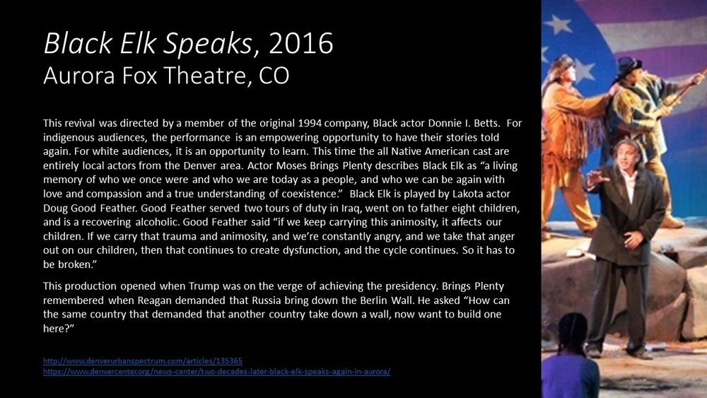 This slide contains one image of the revival of Black Elk Speaks.  Doug Good Feather plays Black Elk.  He is wearing a modern black suit with a white shirt and is addressing the audience directly.  He is standing on a stage that has been designed to look like a rocky outdoor scene with American flag waving in the background. Behind Black Elk are two actors dressed as early pioneers in buckskin clothing. In the foreground is a child with her hair in two braids wearing a blue shirt who is sitting on the ground listening to Black Elk speak.