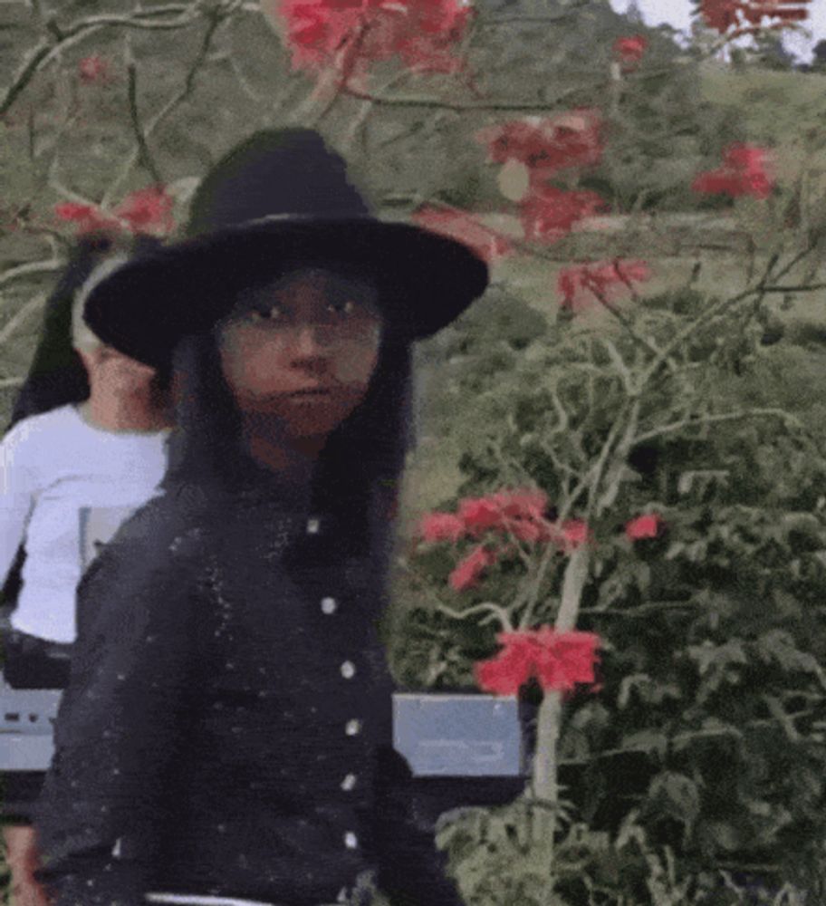 a woman wearing a black hat and a black shirt is standing in front of a piano .