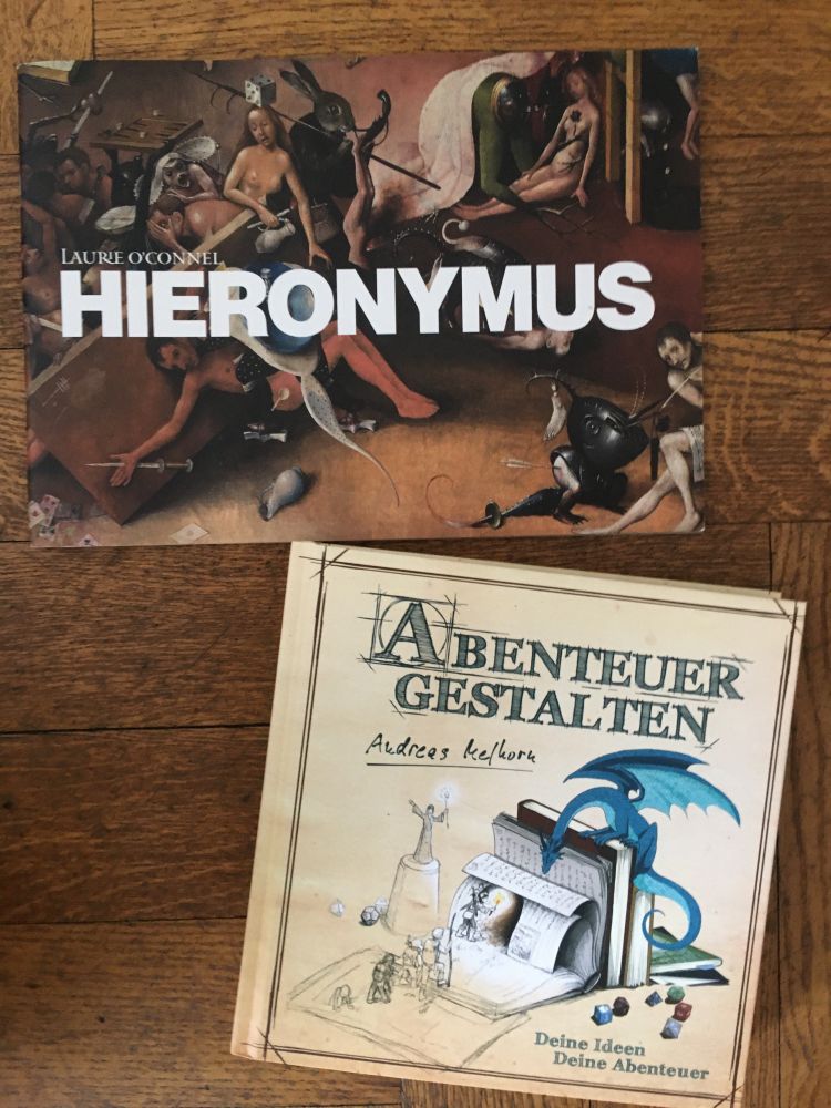 The cover of Hieronymus, which shows a scene from a Hieronymus Bosch painting, and Abenteuer Gestalten, which is a sketch of a bunch of books with dice next to them, and there are adventurers entering the books and becoming more solid looking while a cute blue dragon sits on the books guarding them I guess.