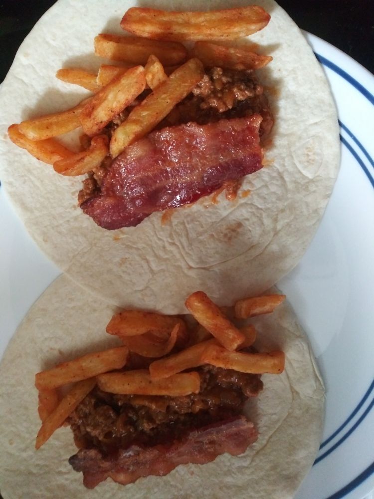 Two fajita sized tortillas with sloppy joe meat, bacon, and fries on them. Consumption imminent.
