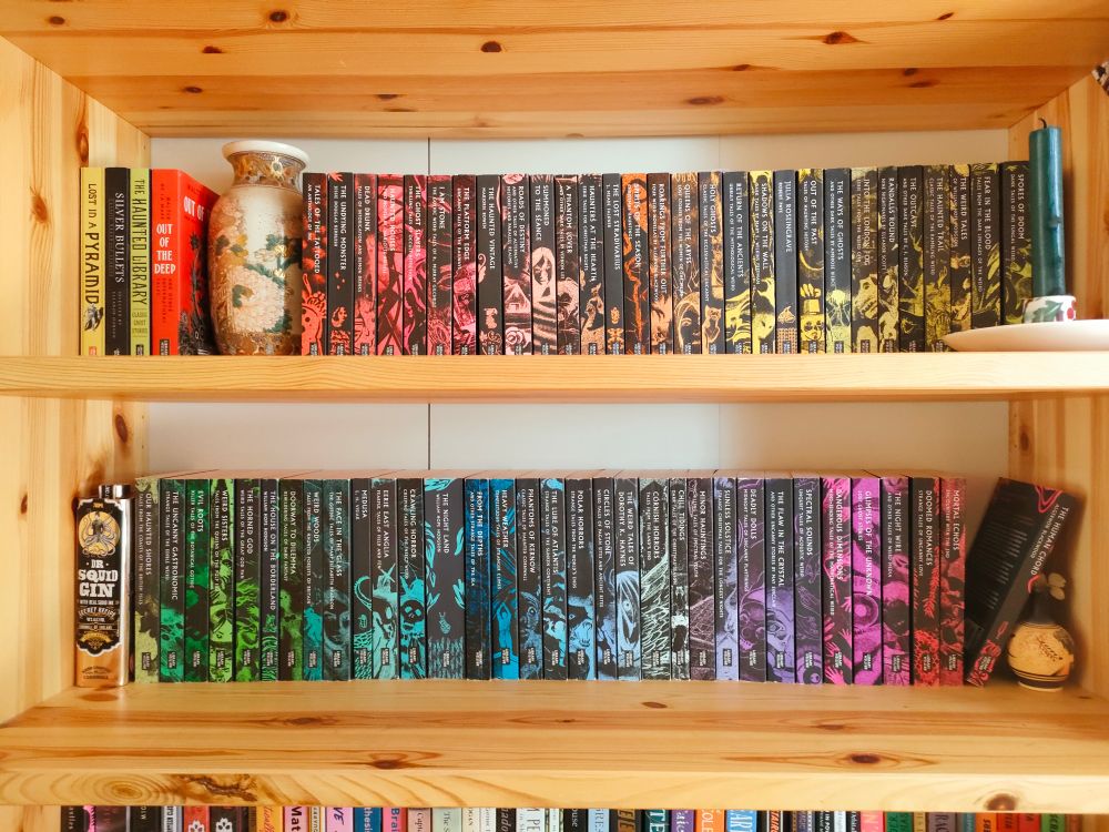 Two bookshelves filled with the British library weird collection arranged in a rough colour spectrum 