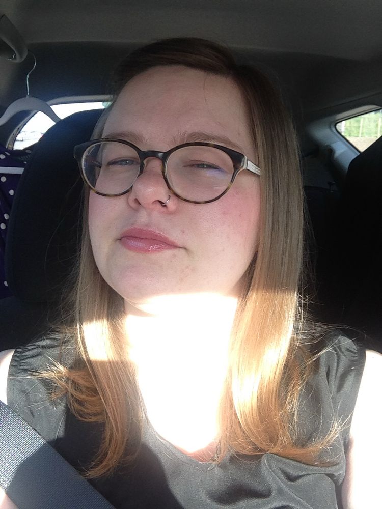 A young white woman with shoulder-length straight blond hair squinting into the sun from the car