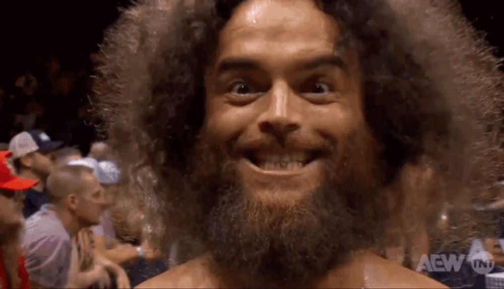 a man with a beard and curly hair is smiling in front of a crowd of people .