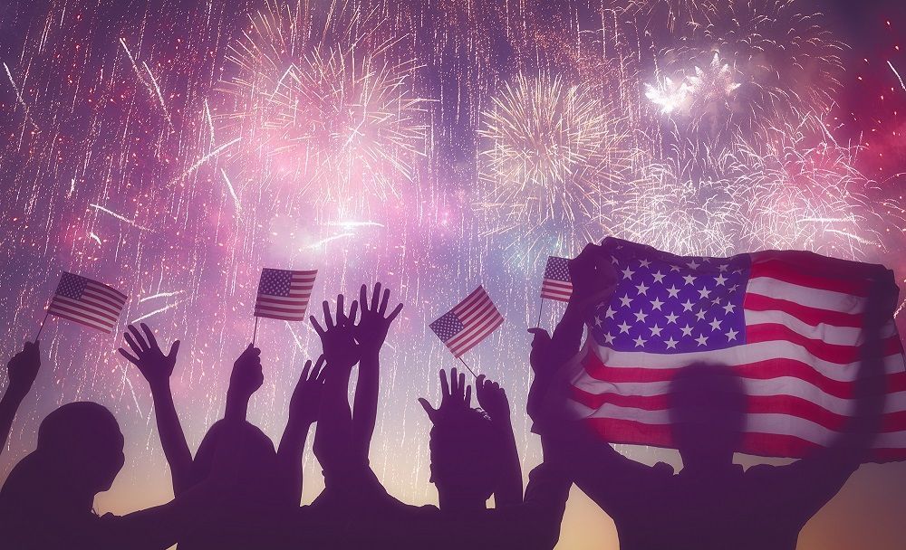Image of night with fireworks in the sky and silhouettes of people watching and waving American flags