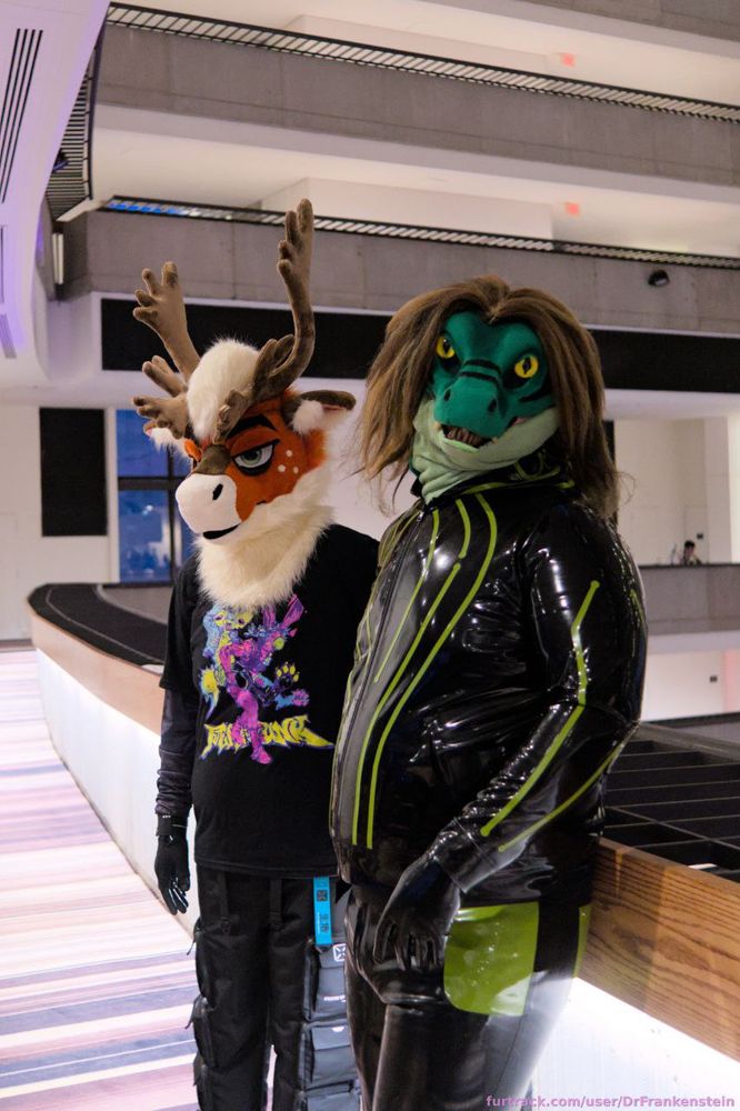Picture of a caribou fursuiter wearing techwear pants and a graphic tee (left) standing next to a green raptor fursuiter wearing a striped latex jacket