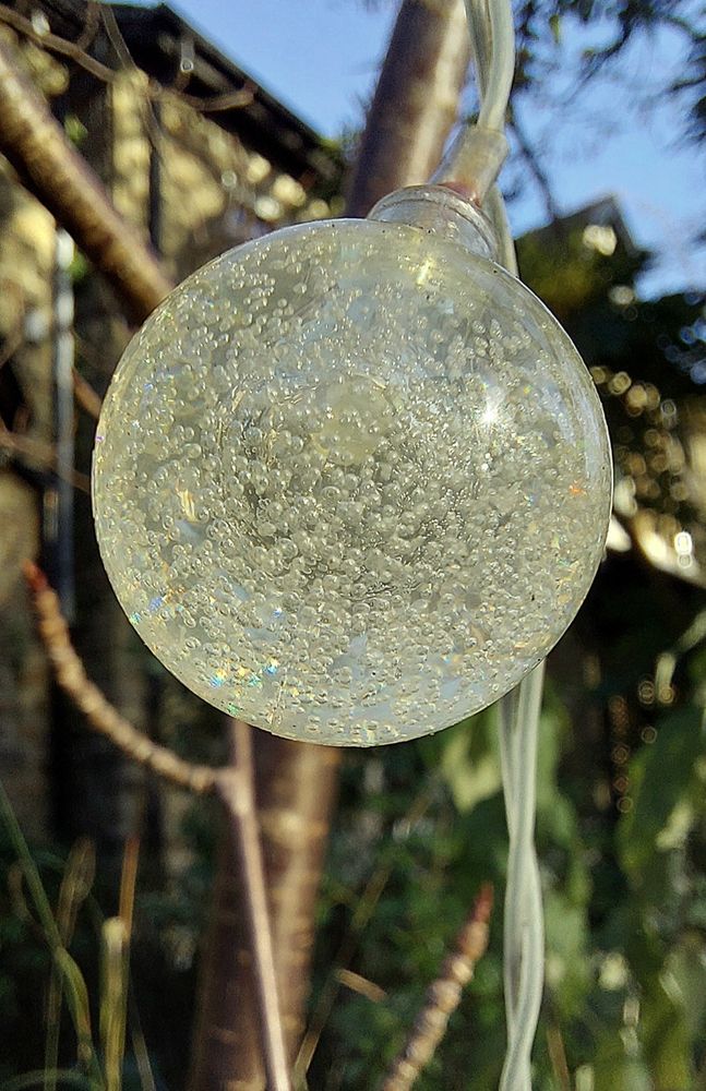 A close up of a small, round clear glass light, unlit but catching the sun. Within the glass are lots of tiny bubbles. 
