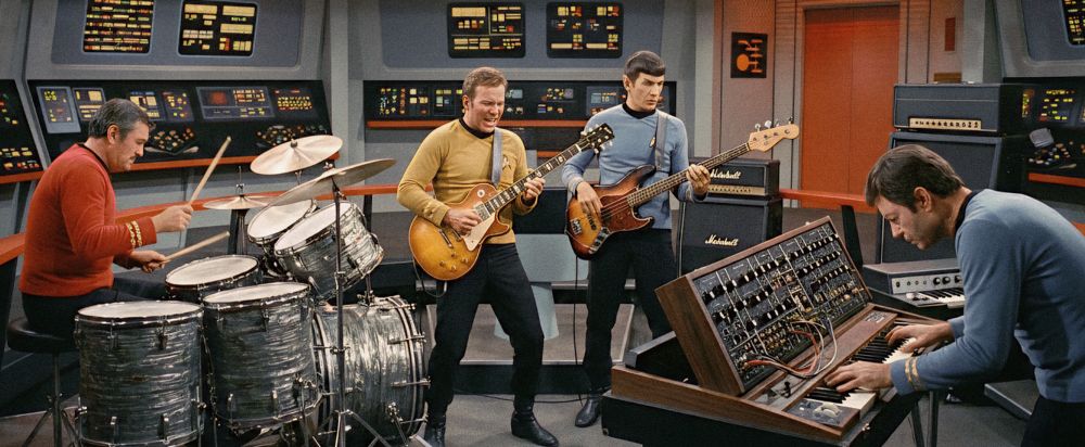 A rock band consisting of Captain Kirk on guitar, Mr. Spock on bass, Scotty on drums, and Dr. McCoy on keyboards, performing on the bridge of the Enterprise