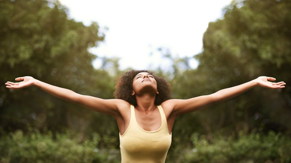 A person smiles with eyes closed and arms outstretched.