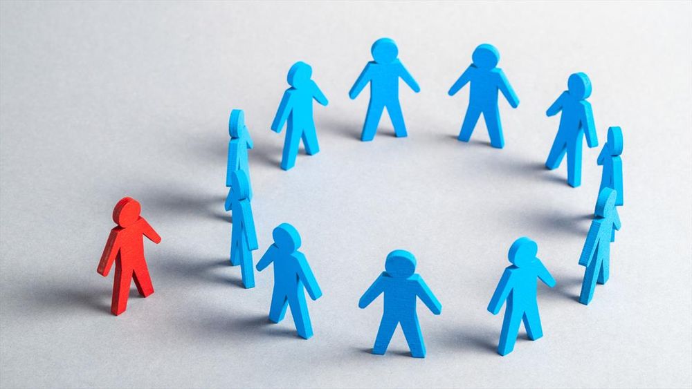 A circle of blue characters with a red character standing outside, indicating exclusion.