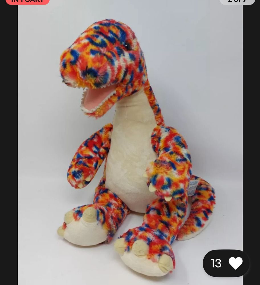 A build a bear dinosaur sitting in front of a white background. He is a diplodocus with rainbow confetti colored fur. 