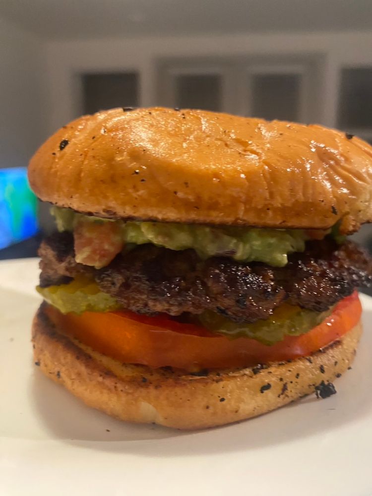 Burger with pickles big slice of tomato, guacamole, and some tasty toasted buns. 