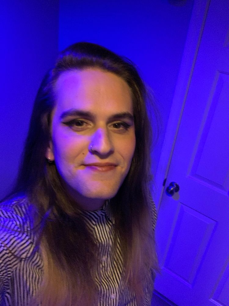 it’s a picture of M, she’s wearing a striped shirt and she’s in a room with blue lighting 