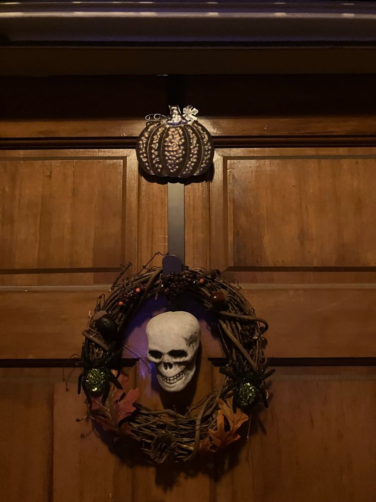 Pumpkin wreath hanger supporting a fall wreath with a skull in the middle. 