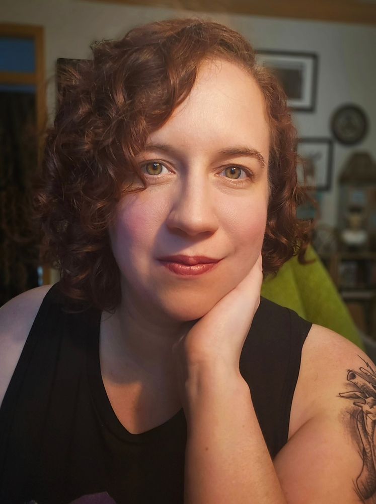 Selfie of a woman with curly hair wearing a black muscle shirt.