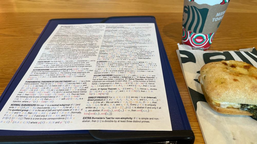 A formula sheet for abstract algebra next to a breakfast sandwich and coffee.